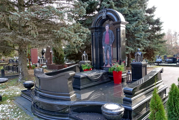 Гранитное надгробье в форме резной арки и укрытая покрывалом плита